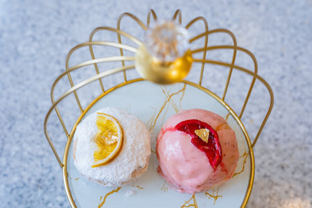 Filled donuts with orange and strawberry toppings and a gold leaf on top. Strawberry Cake Glazed Donuts. Doughnuts with jam filling in golden bird cageの写真素材