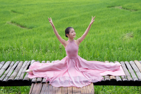 Young woman ballerina in a pink ballet skirt dancing in pointe shoes in a nature. Young beautiful girl doing gymnastic near the green rice fieldの写真素材
