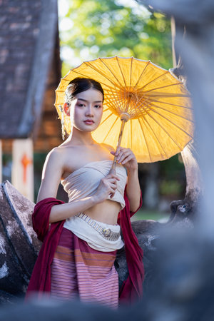 Young beautiful Asian woman wearing thai traditional dress holding umbrella in hand walking at ancient temple with old pagoda in Chiang Mai, Thailandの写真素材