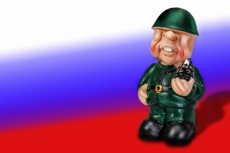 The sullen figure of a soldier in uniform in the helmet with a grenade in hand on background of the flag of Russiaの写真素材