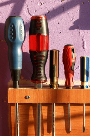 A set of various screwdrivers in a wooden self-made holder on the wallの写真素材