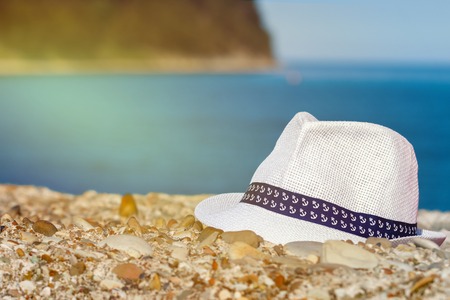 Mens hat of white color lies on stones against the background of the sea and mountainsの写真素材