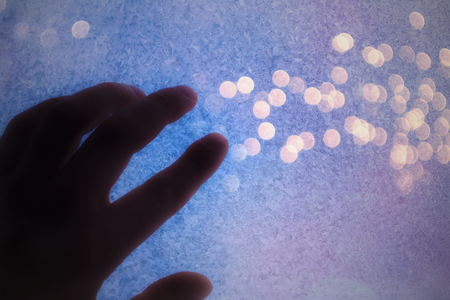 Silhouette of a hand against the night city lights through a frozen window. Copy-spaceの写真素材