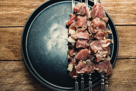 Pieces of raw meat are strung on skewers. Close-up with space for copy. View from above. Black dish with BBQ meat on wooden background. Blank for recipe or menu.の写真素材