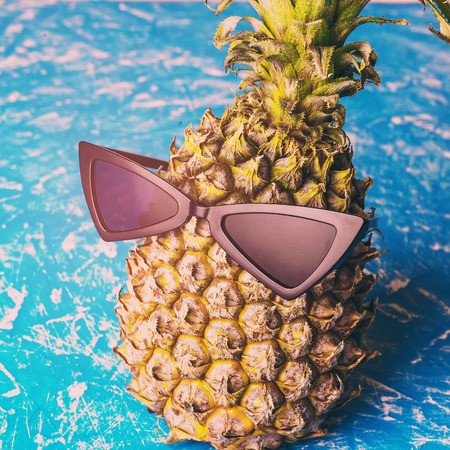 Ripe pineapple in black sunglasses on blue background.  Tropical fruit close up.