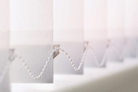 A row of white vertical blinds  cover the sunlight from the window. Close-up with copy spaceの写真素材