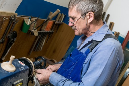 A white elderly man with glasses works at a lathe in a carpentry workshop. The concept of increasing the retirement ageの写真素材
