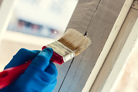 A gloved hand paints a window frame. Repair in the house. Services painter.の写真素材
