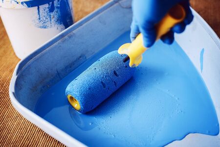 Gloved hand lowers the roller in the tray with blue paint. Services painter. Repair and decoration of apartments. Top viewの写真素材