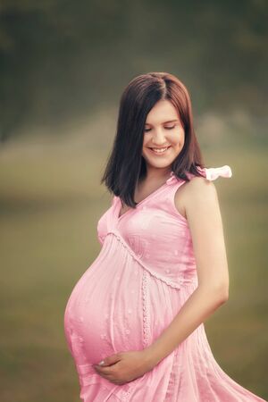 White beautiful pregnant girl in a dress with loose hair in nature. A young girl is happy waiting for a babyの写真素材
