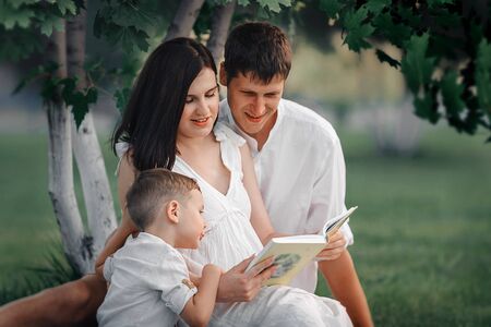 Happy family in nature. Mom, dad and child reading a book under a tree.の写真素材