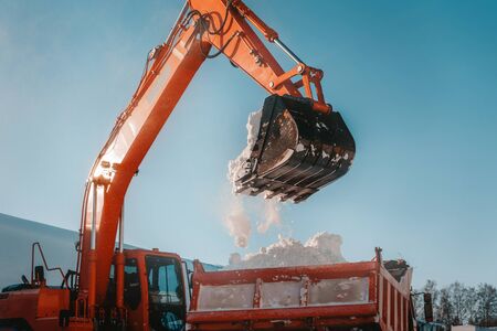 Snow removal after snowfall and blizzards. Excavator loads snow into a truckの写真素材
