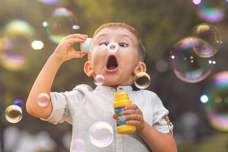 A child with an open mouth and big eyes blows colorful soap bubbles in natureの写真素材