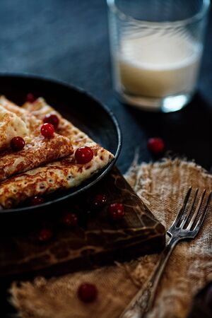 Delicious home-cooked food. Pancakes in a frying pan with cranberry berries and milk. National Russian cuisine. Ready lunch. Rustic style.の写真素材