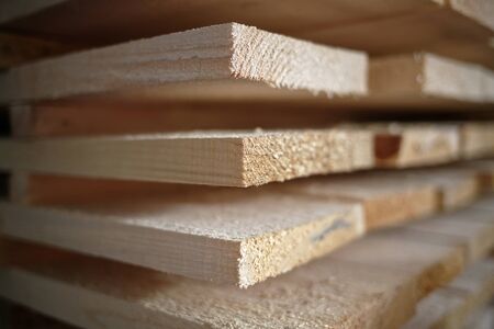 Stack of natural rough wooden boards close-up. Storage of wood in a carpenters workshop or at a sawmillの写真素材