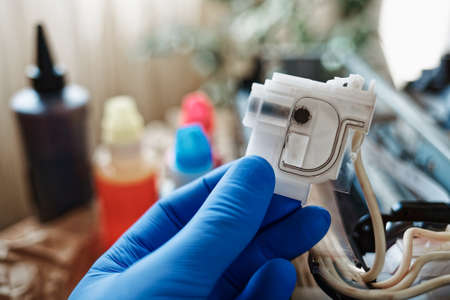Refilling the printer with ink. A gloved hand holds an empty toner container. Service and maintenance of equipment at home. Close upの写真素材