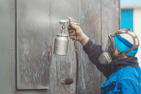 Industrial work. Priming of metal products from the compressor gun. A worker in overalls and a respirator paints the body of a truck trailerの写真素材