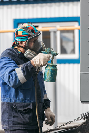 Industrial work. Priming of metal products from the compressor gun. A worker in overalls and a...