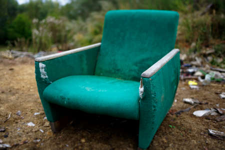 The old chair is in a landfill. Abandoned wasteland with waste and garbage. A symbol of former greatnessの写真素材