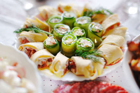 On the festive table is a plate with a delicious snack. Pancake rolls with fish and cucumber...
