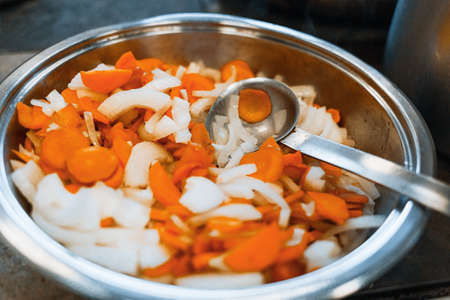 Carrots and onions are stewed in a large shiny plate on the stove. Vegetables are prepared for eating. Close upの写真素材