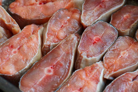 Sliced pieces of red fish are arranged in a row. Abstract background of chum salmon or pink salmon close-up. Backdrop for fish productsの写真素材