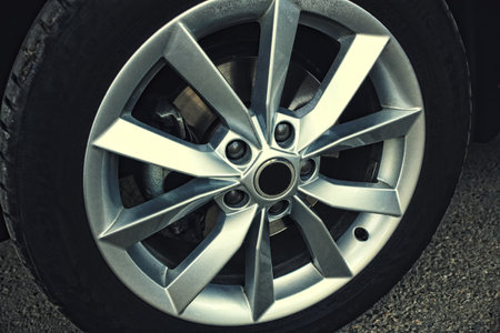 New car wheel with alloy wheel. Detail of the car on a gray asphalt background.