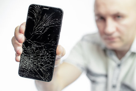 Phone With A broken screen close-up. A white man is holding a black smartphone with a cracked display.の写真素材