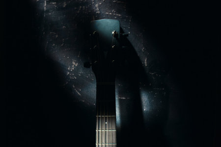 An acoustic guitar stands against the wall against a dark background. Background