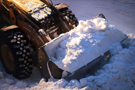 Excavator with a full bucket of snow. Snow removal from city streets at night.