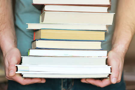A man holds a stack of books in his hands. A photo without a face. A lover of reading.の写真素材