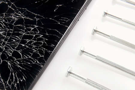 A broken smartphone screen with cracks lies next to the screwdrivers. Close-up.
