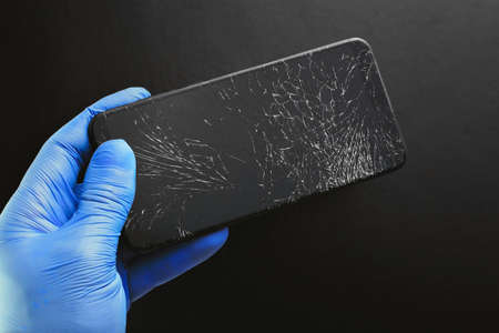 A broken touch phone with a cracked screen in your hand on a black background.の写真素材
