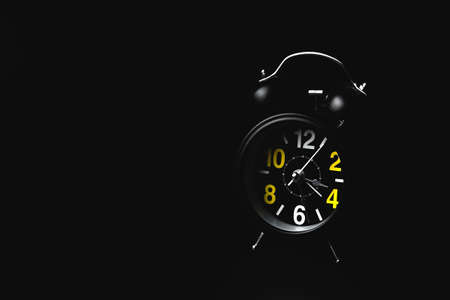 Black round modern alarm clock on black background with copy space. The concept of insomnia and...