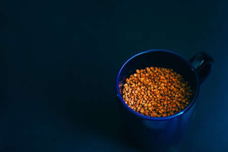 Buckwheat is poured into a blue glass. Top view on a dark background with space to copy. Healthy and healthy food for vegetarians.の写真素材