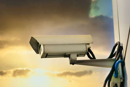 This is a security camera hanging on the wall of a building against the backdrop of a dramatic...