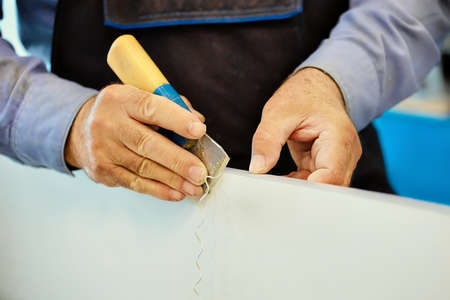 The hands of an elderly carpenter and a tool while working in close-up. Processing of a wooden plate with a cutter in a furniture shop. Close-up. working in a carpentry shopの写真素材