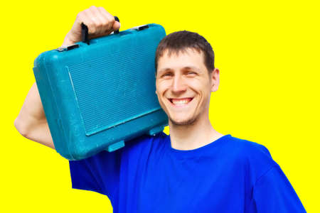 Portrait of a positive young repairman on a yellow background with a wide smile. A worker of Caucasian appearance holds a tool case on his shoulder. Urgent repairs on call. Mockupの写真素材