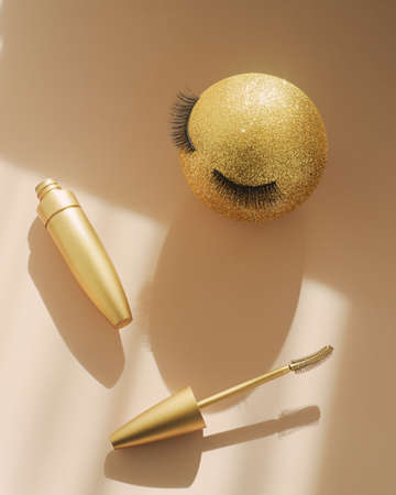 Mascara and a golden Christmas ball with false eyelashes. The concept of festive makeup for women. Make-up artist servicesの写真素材