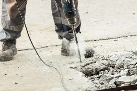 A worker repairs the road surface with a jackhammer on a summer day. Construction works on the road. Industrial background.の写真素材