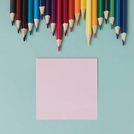 Colored pencils and a sheet for notes lie on a blue background. Top view. Background to-do list back...