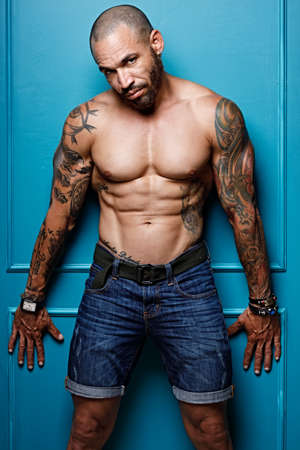 Studio portrait of a muscular African American or Latino with a naked torso. Male strength and potency. Brutal man with tattoos on his body. Strong muscles.の写真素材