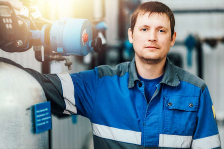 Portrait of a young Caucasian worker in overalls against the background of boiler equipment....