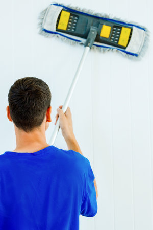 A young Caucasian man in a blue T-shirt washes the white wall of the room with a mop. Clearing...