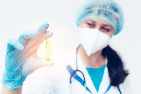 A medical woman holds an ampoule with a vaccine or medicine in her hand and looks at it. A new vaccine. Preparation for vaccination.の写真素材