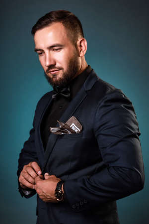 An elegant business man fastens a classic jacket. Studio portrait of a Caucasian entrepreneur or...