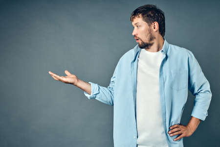 A white Caucasian man with a beard stands on a gray background and looks at an empty palm in surprise. Studio portrait for advertising a product or service. Space to copy. Layoutの写真素材