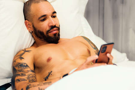 A bearded man lies in the post and corresponds on the phone. A sexy Cuban with a naked torso looks...