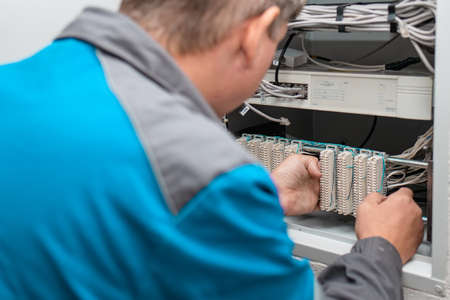 A man electrician checks the terminals of telephone communication equipment. The specialist serves...