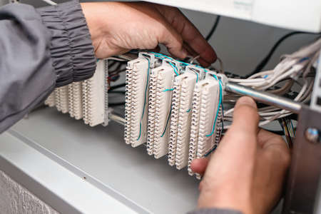 A man electrician checks the terminals of telephone communication equipment. The specialist serves...